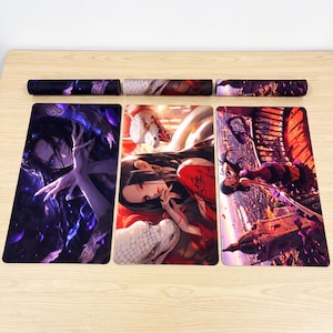May include: Three rectangular desk mats featuring vibrant anime-style illustrations. The left mat shows a character with dark hair in a purple-toned scene. The centre mat depicts a character with a white snake. The right mat shows a character on a balcony.