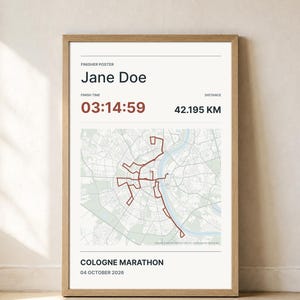 Könnte beinhalten: Ein gerahmtes Finisher-Poster für den Köln-Marathon mit dem Namen Jane Doe, einer Zielzeit von 03:14:59, einer Distanz von 42,195 KM, dem Datum 04. Oktober 2026 und einer roten Routenkarte der Stadtstraßen auf hellem Hintergrund.