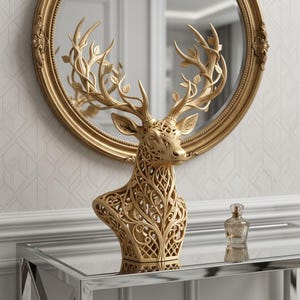 May include: A gold-coloured deer bust sculpture featuring an intricate, openwork filigree design of swirling vines and leaves throughout the neck and antlers. The deer is positioned in front of a large, round, gold-framed mirror on a glass table.