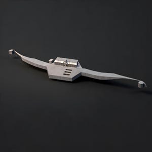 May include: A gray, elongated, symmetrical object with a central rectangular structure featuring a small house-like roof. The base has three horizontal cutouts, and the ends taper into thin arms, one ending in a cube and the other in a cylinder.