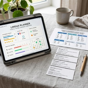 May include: A tablet displaying a Lingua Planner interface with weekly goals, a study log, and a calendar, alongside a printed French grammar cheat sheet, four vocabulary flashcards, and a pen on a textured fabric surface.