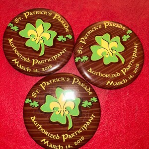 May include: Three round St. Patrick's Parade buttons. Each button has a brown background with a green and yellow shamrock design. The text "St. Patrick's Parade", "Authorized Participant", and "March 14, 2015" are printed on each button.
