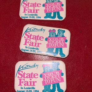 May include: Three rectangular Kentucky State Fair pins. Each pin has the text "Kentucky State Fair" in pink and green, with the dates "August 18-28, 1994." A cartoon bear couple holds a sign that reads "Your Ticket to Fun!"