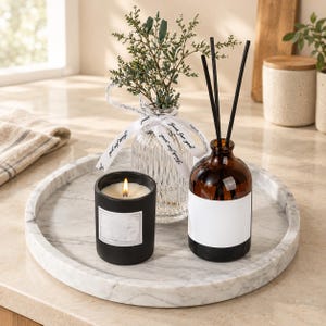 May include: A round white marble tray holding a black candle with a lit wick, a clear ribbed glass vase containing green sprigs tied with a white ribbon printed with the text Just for you, and an amber glass reed diffuser with black sticks.
