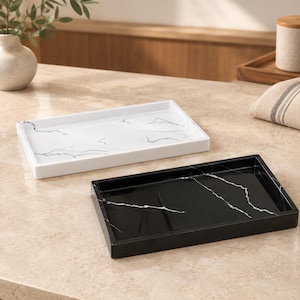 May include: Two rectangular trays with raised edges, one in white with black veining and one in black with white veining. Both trays feature a smooth, polished finish and a marble-like pattern, designed for holding small items on a flat surface.