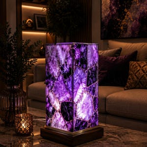 May include: A rectangular table lamp featuring a mosaic of translucent purple amethyst stone slices illuminated from within, set upon a dark wooden base. The lamp emits a vibrant violet glow, highlighting the crystalline textures and jagged edges.