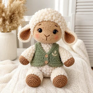 May include: A crocheted stuffed lamb toy with cream-colored textured wool, brown hooves, and a tan face. The lamb wears a sage green crocheted vest featuring two small wooden buttons and a small embroidered leaf detail on the chest.