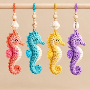 Puede incluir: Cuatro adornos de caballitos de mar tejidos a ganchillo en coral, turquesa, amarillo y morado. Cada caballito tiene una barriga blanca, una pequeña aleta lateral y una cola enroscada, colgados de bucles de hilo con una cuenta de madera y una concha.