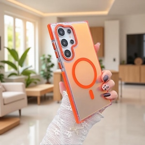 May include: A rectangular smartphone case with a translucent frosted back and a vibrant orange frame. The case features a prominent orange circular magnetic charging ring on the back and a raised orange camera module housing five circular lenses.