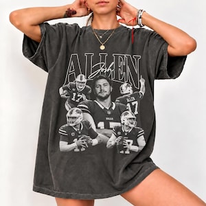 May include: A charcoal grey oversized t-shirt featuring a vintage-style graphic print of football player Josh Allen. The design includes the name ALLEN in large block letters, a script signature, and four black and white action photos of the player.