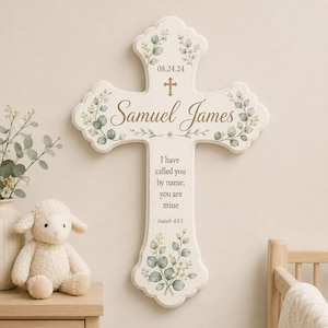May include: A white wall-mounted cross featuring green eucalyptus leaf illustrations, the name Samuel James, the date 08.24.24, and the text I have called you by name; you are mine Isaiah 43:1 in brown lettering with a small gold cross icon.