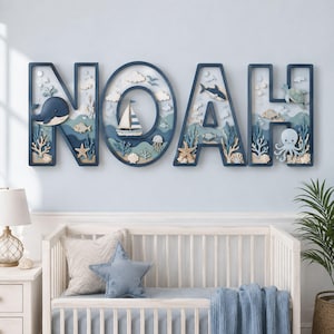 Puede incluir: Un letrero de madera para pared que deletrea el nombre NOAH en letras mayúsculas de color azul oscuro. Cada letra presenta una escena oceánica tridimensional en capas con una ballena, velero, tiburón, tortuga, pulpo, estrellas y corales.