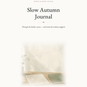 May include: A white journal cover titled Slow Autumn Journal by North & Mind Studio. The text reads: Through the darker season &mdash; with what the evidence supports. Below, a small green book and a white paper rest on a wooden surface with 28 writing prompts - 8 chapters - grounded in psychology.