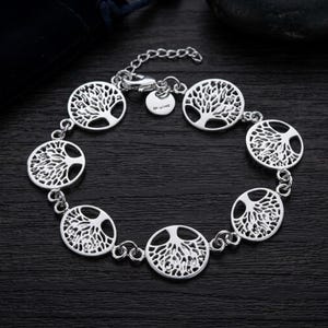 May include: A silver-toned chain bracelet featuring six circular charms, each displaying an intricate cutout design of a tree with spreading branches and roots. The bracelet includes a lobster claw clasp, an adjustable extender chain, and a small round tag.