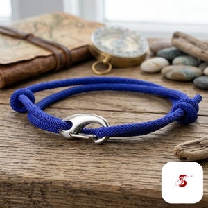 May include: A vibrant blue cord bracelet featuring a polished silver-tone metal hook clasp. The bracelet is constructed from a durable, woven synthetic rope material with two adjustable sliding knots on either side of the central metal hook closure.