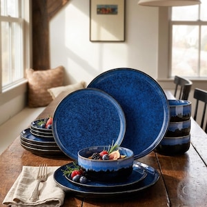 May include: A set of dark blue ceramic dinnerware featuring a mottled, speckled finish. The collection includes large dinner plates, smaller salad plates, and deep bowls with a smooth, glossy glaze and a dark, solid-colored base rim.