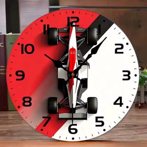Op de afbeelding: Een ronde wandklok met een gespleten rood en wit achtergrondontwerp en een centrale afbeelding van een Formule 1-raceauto. De wijzerplaat toont zwarte Arabische cijfers van 1 tot 12, met zwarte uur- en minutenwijzers en een rode secondewijzer.