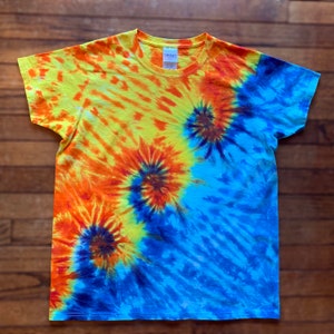 May include: A tie-dye t-shirt with a spiral pattern in yellow, orange, and blue. The crew neck t-shirt is made of a soft material. The design is a vibrant example of textile art.