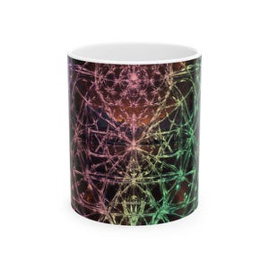 May include: A cylindrical ceramic mug featuring a vibrant, multi-colored fractal pattern that transitions from pink and orange hues to shades of green. The intricate geometric design covers the exterior surface, while the interior is solid white.