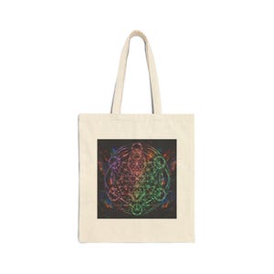 May include: A beige canvas tote bag featuring a square graphic print on the front. The print displays a complex, multicoloured geometric pattern with intersecting circles and lines in vibrant hues of red, green, blue, and purple on a black background.