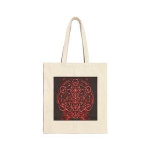 May include: A beige canvas tote bag featuring a centred square graphic print. The design displays a complex, glowing red geometric pattern composed of intersecting circles and lines, resembling a sacred geometry motif on a dark background.