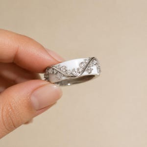 May include: A white ceramic ring featuring a silver-toned metal overlay with a vine-like pattern. The metal design is embellished with small, clear, round-cut stones set along the winding branches that wrap around the smooth white band.