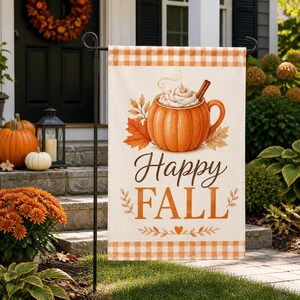 May include: A rectangular garden flag featuring a cream background with orange gingham borders. The design displays a pumpkin-shaped mug filled with whipped cream and a cinnamon stick, surrounded by autumn leaves and the text Happy FALL.