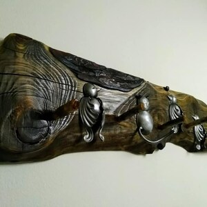 May include: A rustic wooden coat rack with three metal hooks shaped like birds. The wood is dark brown with a natural grain pattern. The hooks are silver and have a detailed design.