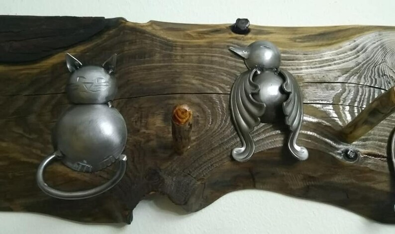 May include: A wooden wall-mounted coat rack with three metal hooks. The hooks are shaped like a cat, a bird, and a simple hook. The wood is dark brown with a natural finish.