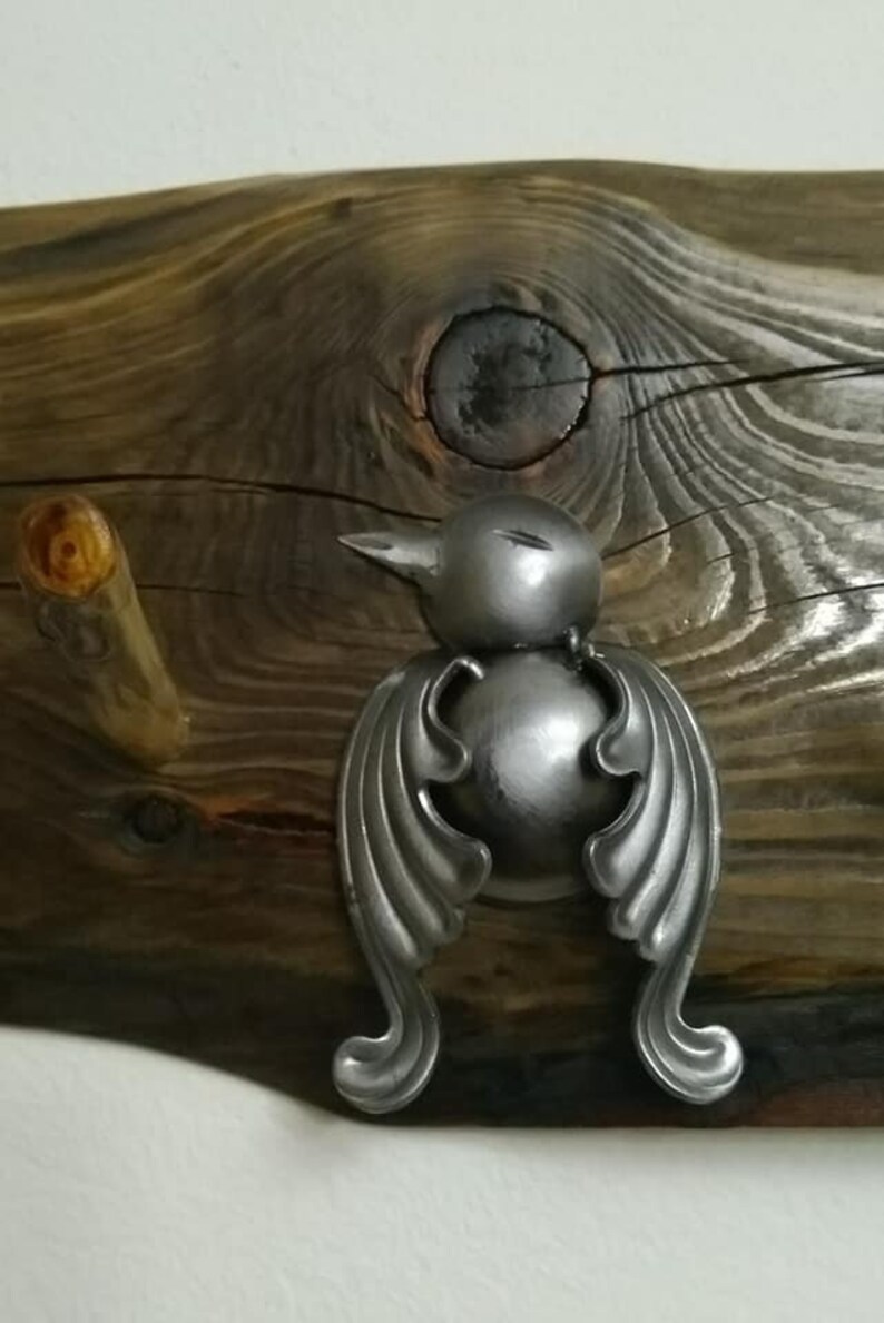 May include: A silver metal bird-shaped hook with wings and a round body, mounted on a rustic wooden surface.