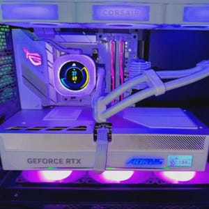 May include: A white computer gaming desktop interior featuring a liquid cooling system with a circular digital display showing 37 and 49, a white graphics card labelled GEFORCE RTX and AORUS, and internal components illuminated by purple and blue lighting.