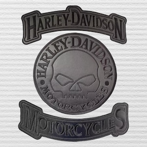May include: A black embroidered patch set featuring a top rocker with the text HARLEY-DAVIDSON, a central circular emblem with a skull graphic and the text HARLEY-DAVIDSON, and a bottom rocker with the text MOTORCYCLES in bold black lettering.