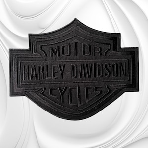 May include: A black embroidered patch featuring the iconic Harley-Davidson shield logo. The design includes the text MOTOR, HARLEY-DAVIDSON, and CYCLES stitched in black thread against a matching black background, creating a monochromatic look.