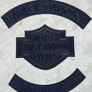 May include: A set of three black embroidered patches featuring the Harley-Davidson logo. The top arched patch reads Harley-Davidson, the center shield patch reads Motor Harley-Davidson Cycles, and the bottom arched patch reads Motorcycles.