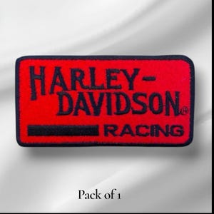 May include: A rectangular embroidered patch with a bright red background and a dark navy blue border. The text Harley-Davidson is stitched in dark navy blue, with the word Racing below it in the same color, accompanied by a horizontal line.
