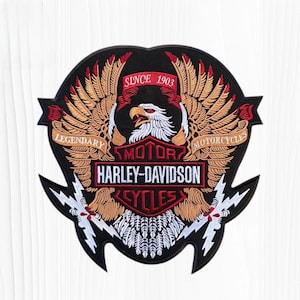 May include: A large embroidered patch featuring a central bald eagle head with spread wings in shades of tan and brown. The design includes red banners with the text SINCE 1903, LEGENDARY MOTORCYCLES, and a central black shield with white text HARLEY-DAVIDSON CYCLES.