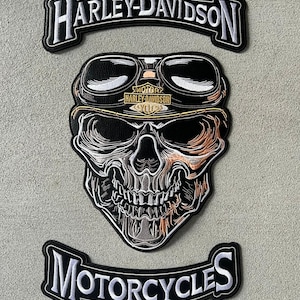 May include: A three-piece embroidered patch set featuring a black and white Harley-Davidson rocker at the top, a central skull wearing goggles with Harley-Davidson branding, and a black and white Motorcycles rocker at the bottom.