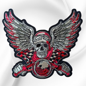 May include: An embroidered patch featuring a central skull wearing aviator goggles and a scarf, flanked by large feathered wings. Below the skull are two crossed checkered racing flags and a circular emblem with a red and black graphic design.