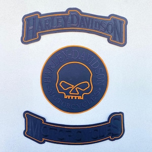 May include: Three black embroidered patches with orange borders. The top arched patch reads Harley-Davidson. The center circular patch features a skull graphic with the text Harley-Davidson Motorcycles. The bottom arched patch reads Motorcycles.