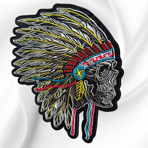 May include: An embroidered patch featuring a skull wearing a large feathered headdress. The design uses black, white, yellow, red, and blue thread to depict the skull and feathers, with a detailed geometric band across the forehead area.
