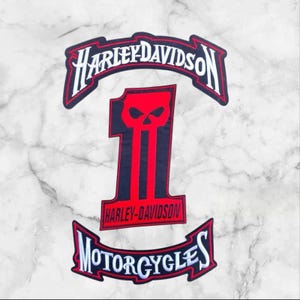 May include: A three-piece embroidered patch set featuring a top rocker with white Harley-Davidson text, a central number one patch with a red skull graphic and Harley-Davidson text, and a bottom rocker with white Motorcycles text on black.