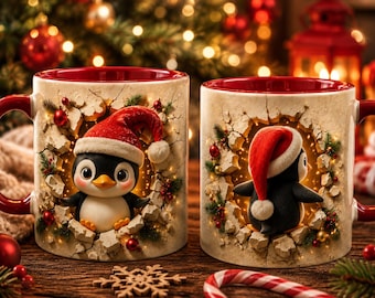 May include: Two ceramic mugs with a red interior and handle, featuring a 3D-effect graphic of a penguin wearing a Santa hat emerging from a cracked wall. The design includes festive greenery, red berries, and warm golden lights around the penguin.