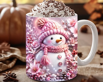 May include: A white ceramic mug featuring a printed illustration of a snowman wearing a pink knit hat and scarf, surrounded by pink flowers, berries, and snowflakes. The mug is filled with whipped cream topped with chocolate shavings.