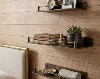 May include: Three rectangular wall-mounted shelves made of dark bronze-toned metal with a horizontal guard rail. The shelves hold a vintage-style alarm clock, a framed photograph, two books titled Meditations and Wanderlust, a succulent, and a towel.