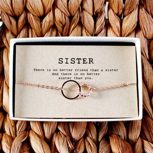 May include: A gift box with a delicate gold chain bracelet featuring two intertwined circles. The box has a card inside with the text "SISTER There is no better friend than a sister And there is no better sister than you."