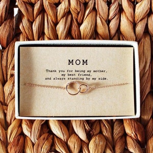 May include: A small gift box with a delicate gold chain necklace featuring two interlocking circles. The box has a card inside with the message "MOM Thank you for being my mother, my best friend, and always standing by my side."