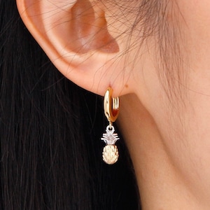 Könnte beinhalten: Goldene Creolen mit einem baumelnden Ananas-Anhänger. Die Ananas ist texturiert und hat eine silberne Spitze.