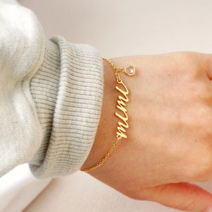 Op de afbeelding: Gouden kettingarmband met een bedel met de tekst "mama" en een klein helder kristal.