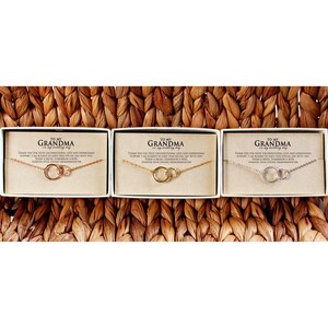 Puede incluir: Tres cajas blancas con collares de oro y plata en su interior. Cada caja tiene un mensaje que dice "A mi abuela en mi d&iacute;a de boda".