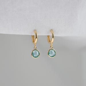 Pode incluir: Brincos de argola de ouro com uma gema azul claro pendurada.